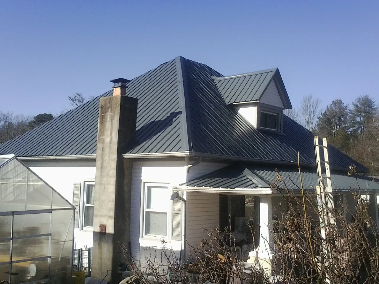 Dark blue standing seam metal roof on a white farmhouse with dormer — Slate & Tile Roof Repair by Roofing Brothers in Accokeek