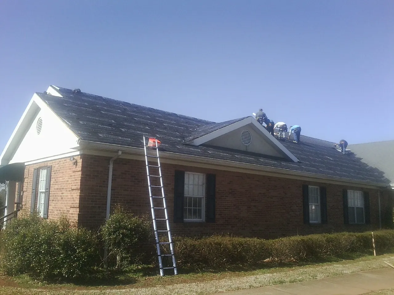 Crew tearing shingles off a brick ranch roof with a ladder set — Emergency Roof Repair work by our crew in Accokeek