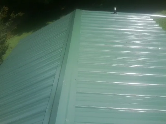 New green metal panels meeting at the ridge of a roof — Flat Roof Repair work by our crew in Accokeek