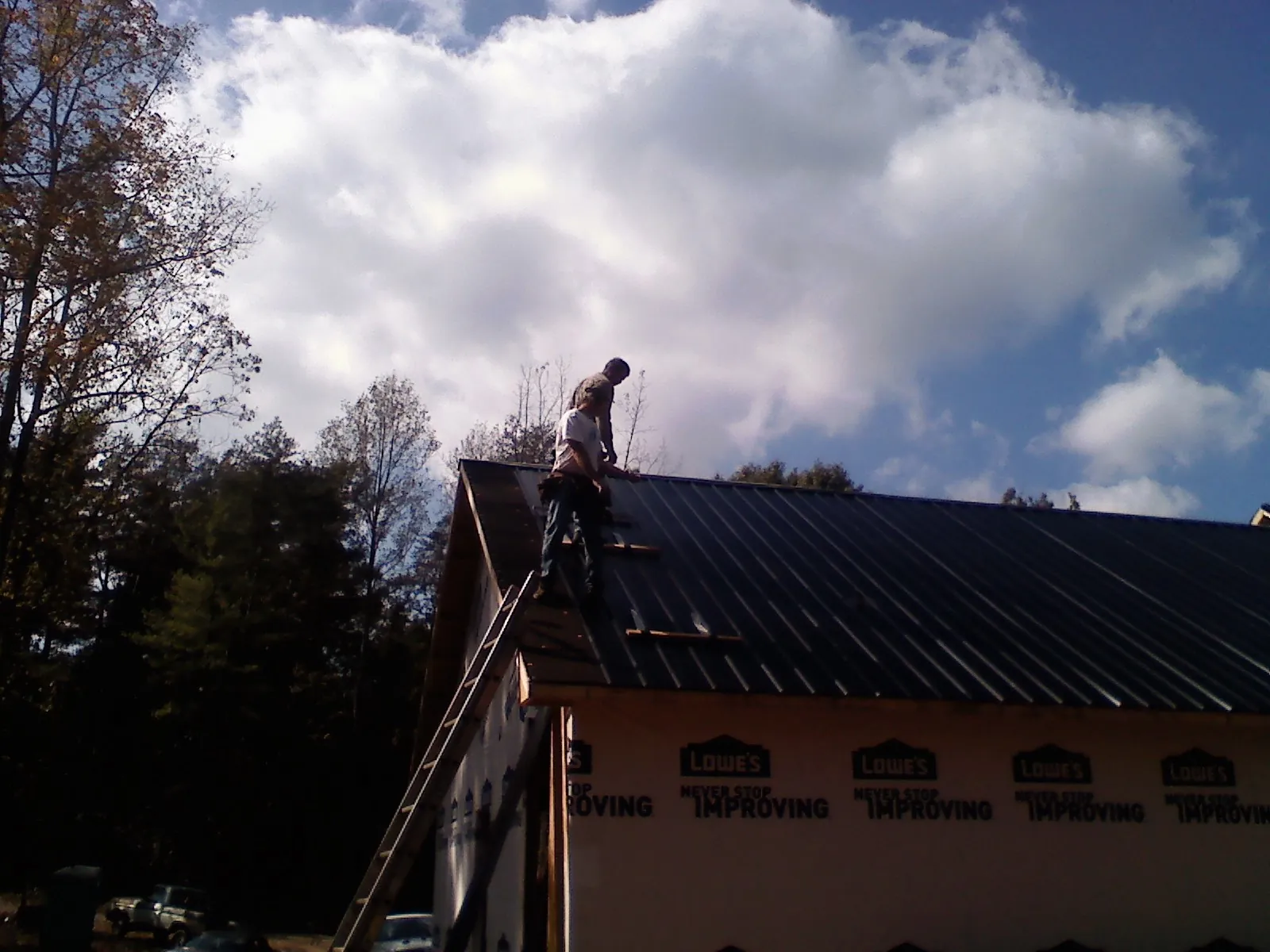 Roofer fastening dark metal panels high against a cloudy sky, from a Roof Inspection job in Accokeek
