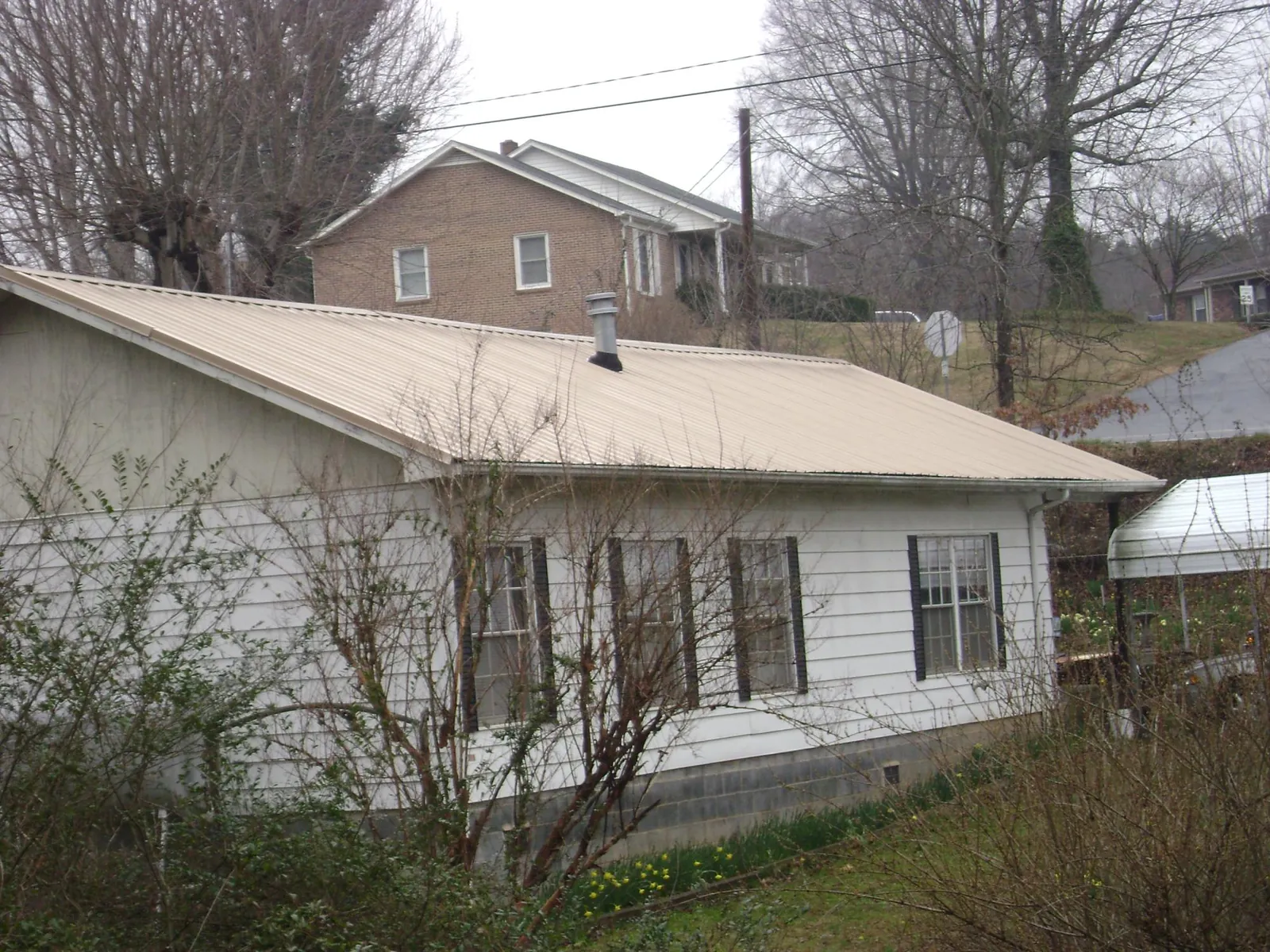 Tan metal roof on a white sided house set into a hillside — Commercial Roofing by Roofing Brothers in Accokeek